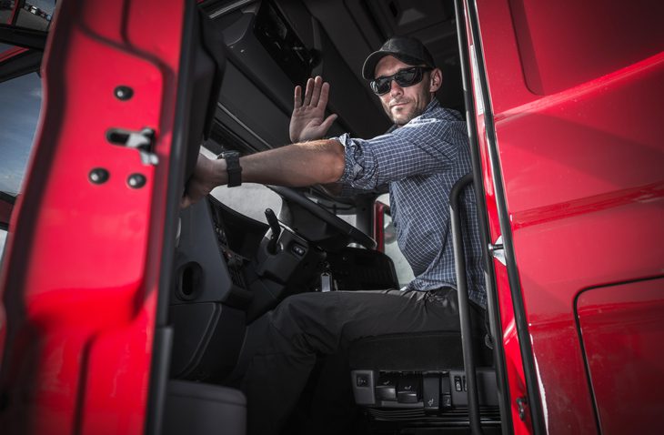 Truck driver waving on his side with an open door of the truck.